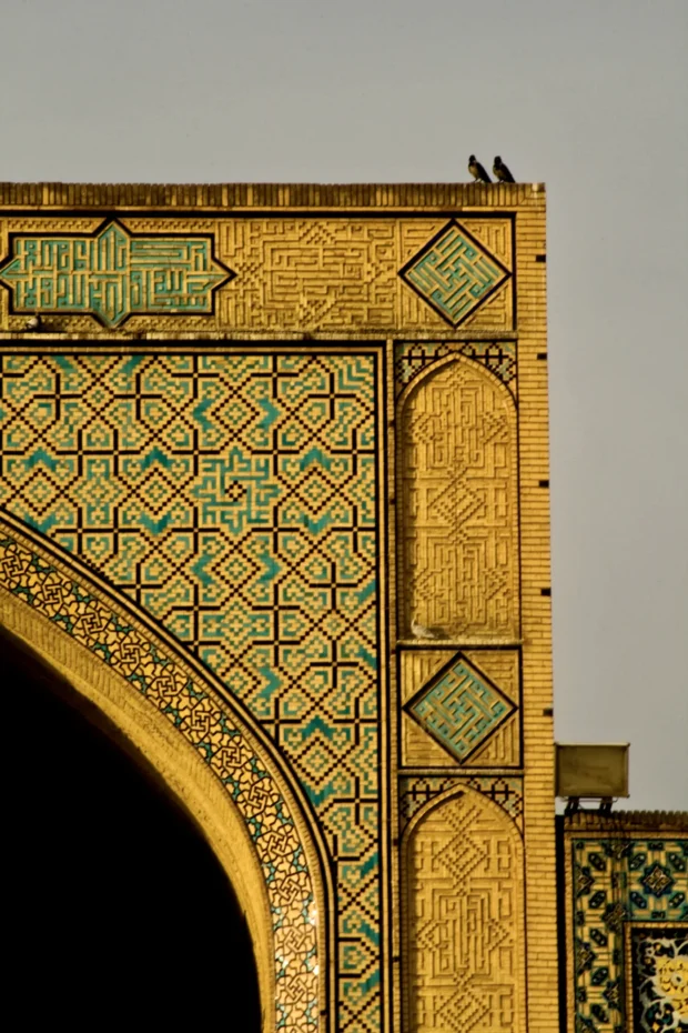 Two birds on the corner of a gold and turquoise tiled arch.
