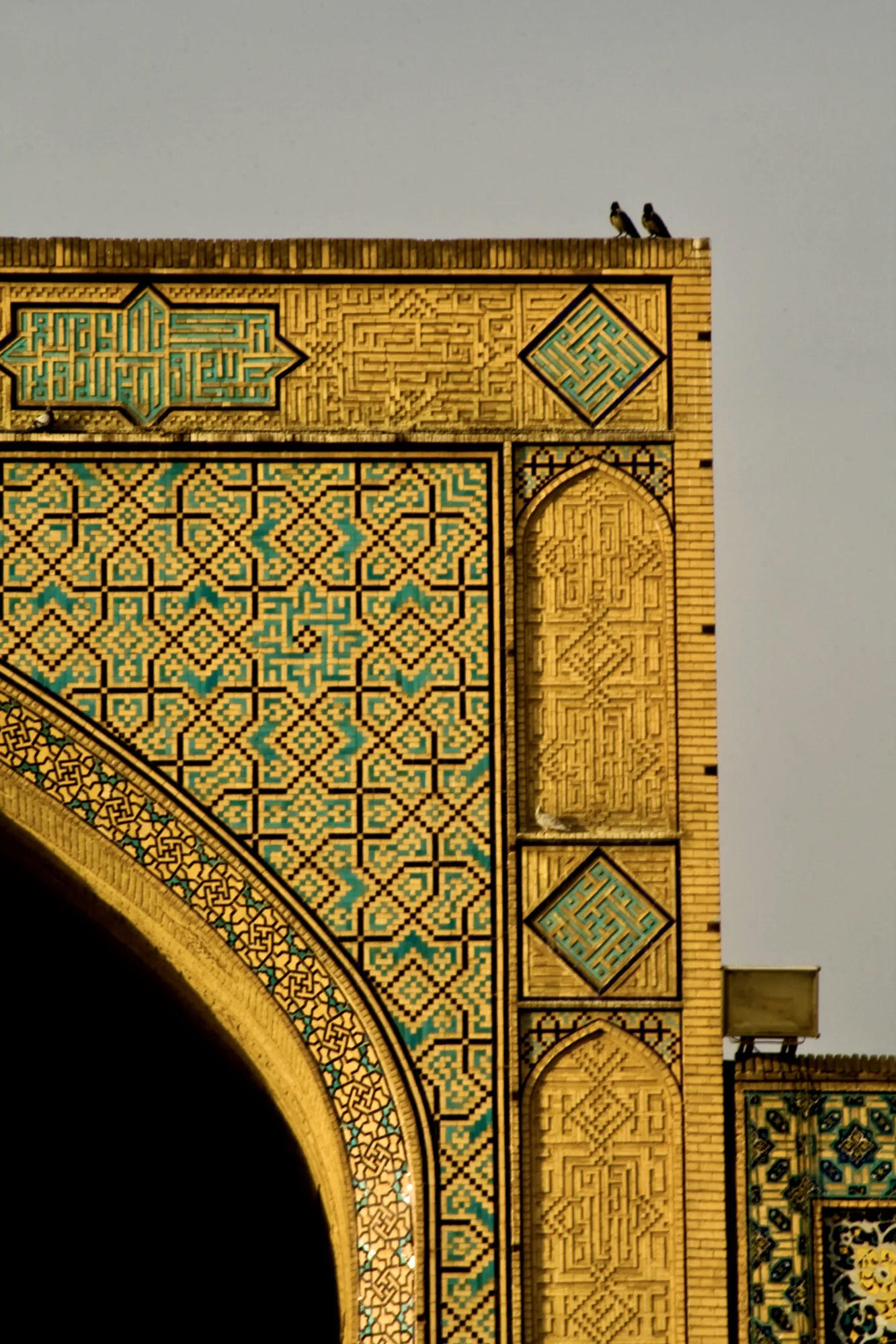 Two birds on the corner of a gold and turquoise tiled arch.
