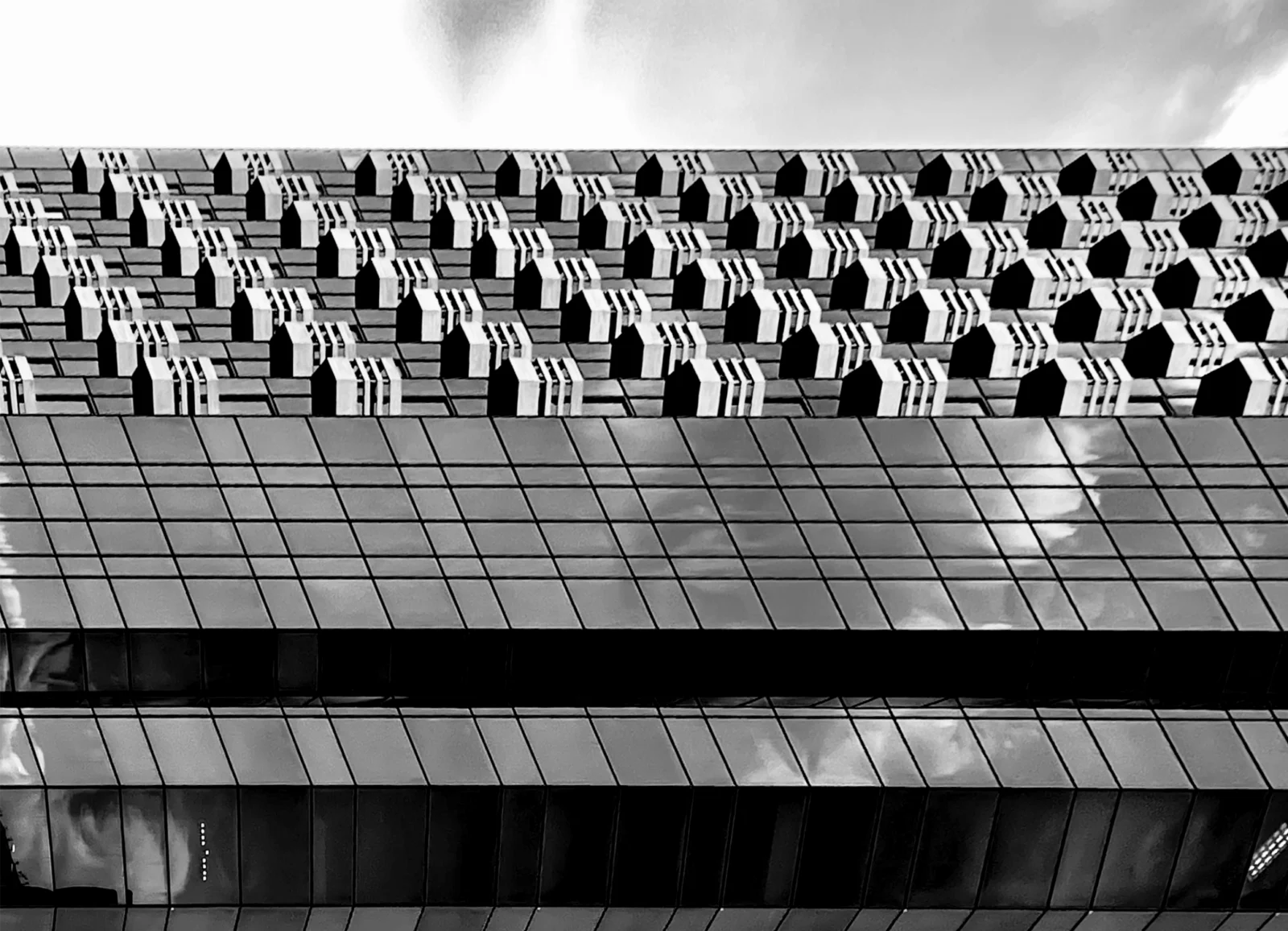 A glass tower beside a perforated concrete screen, black and white.
