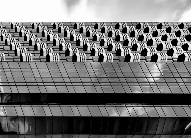 A glass tower beside a perforated concrete screen, black and white.