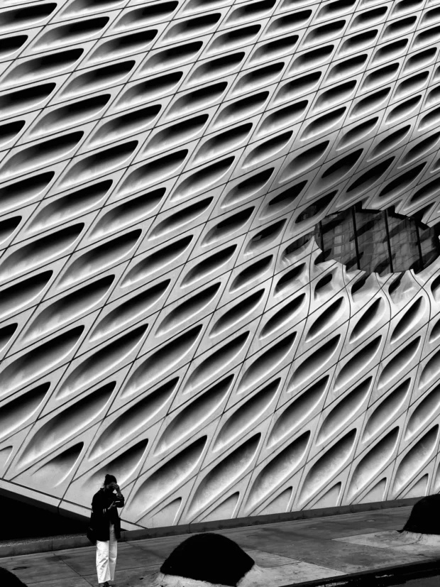 The Broad: the whole diagonal lattice skin with the oculus pressed into it, one person at the base holding the scale.