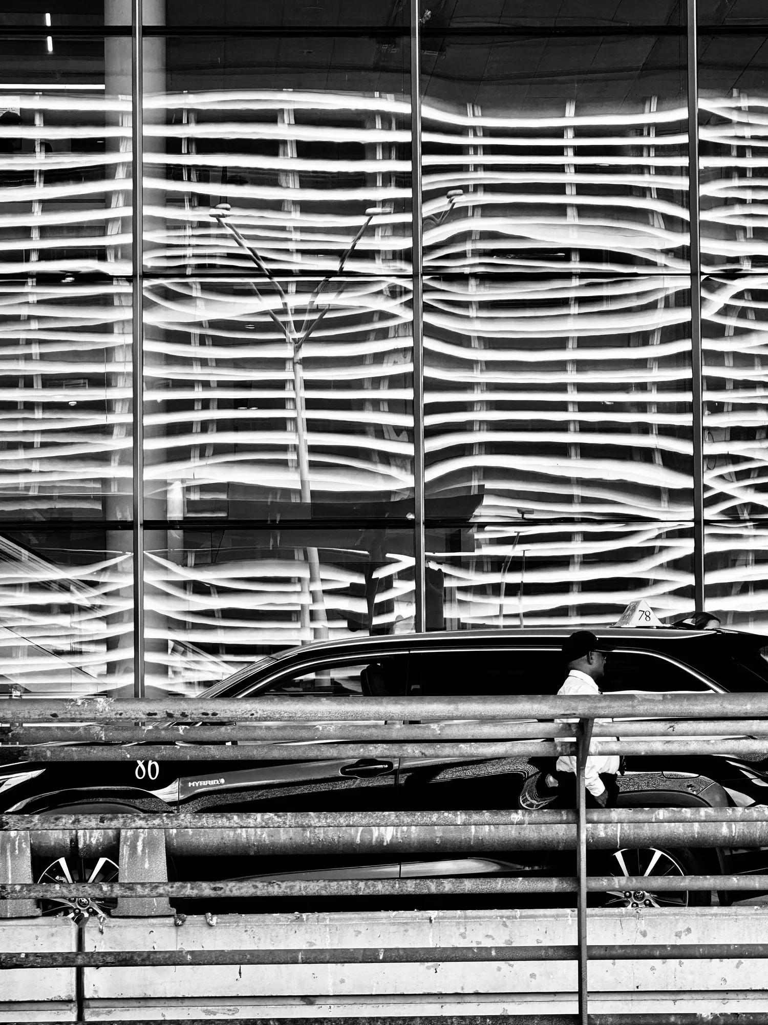 A parking ramp spiral in black and white, the decks stacking into stripes, one car and one person at the foot.