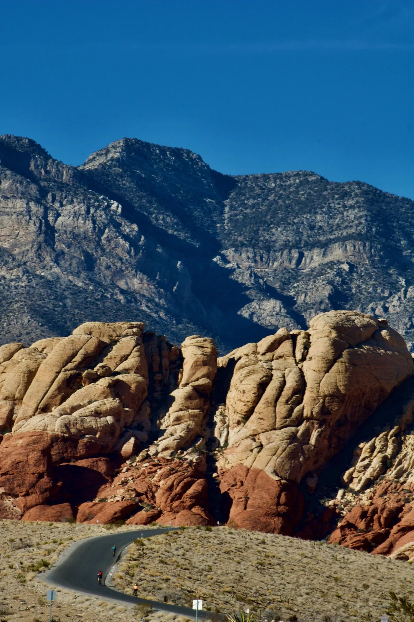 Red rock, a road curving through it, a grey mountain wall behind.