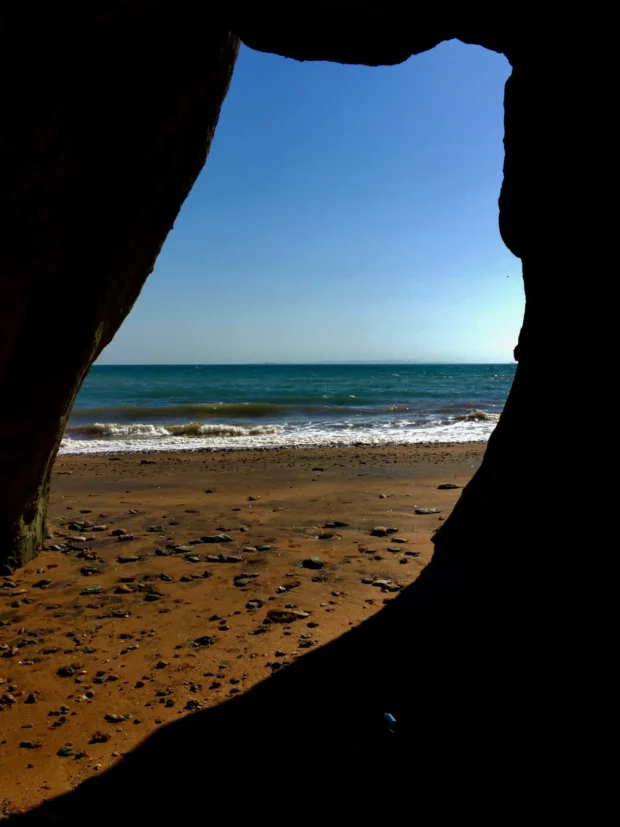 The sea seen through the mouth of a cave, the dark rock around the opening shaped like an owl.