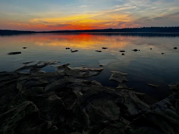 A lake at dusk with a flat rock shelf across the foreground.
