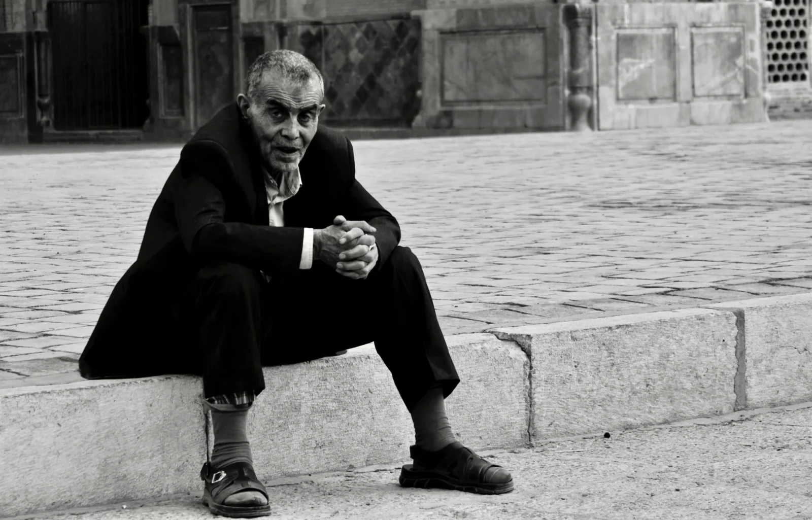 A man smoking on a step, plain pavement, nothing else in the frame.