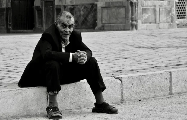 A man smoking on a step, plain pavement, nothing else in the frame.