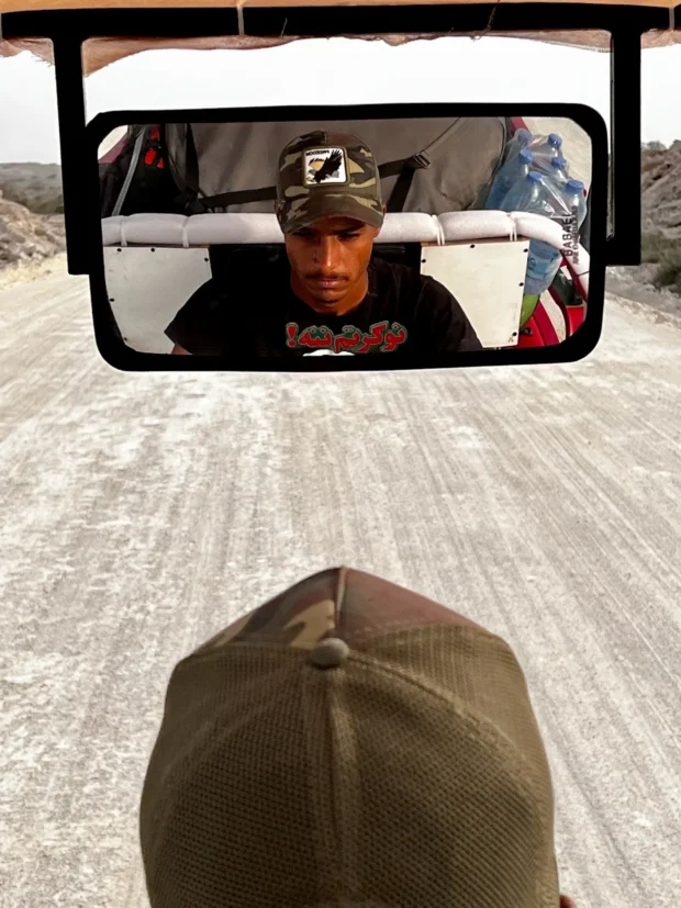 A driver's face framed in the rickshaw mirror.
