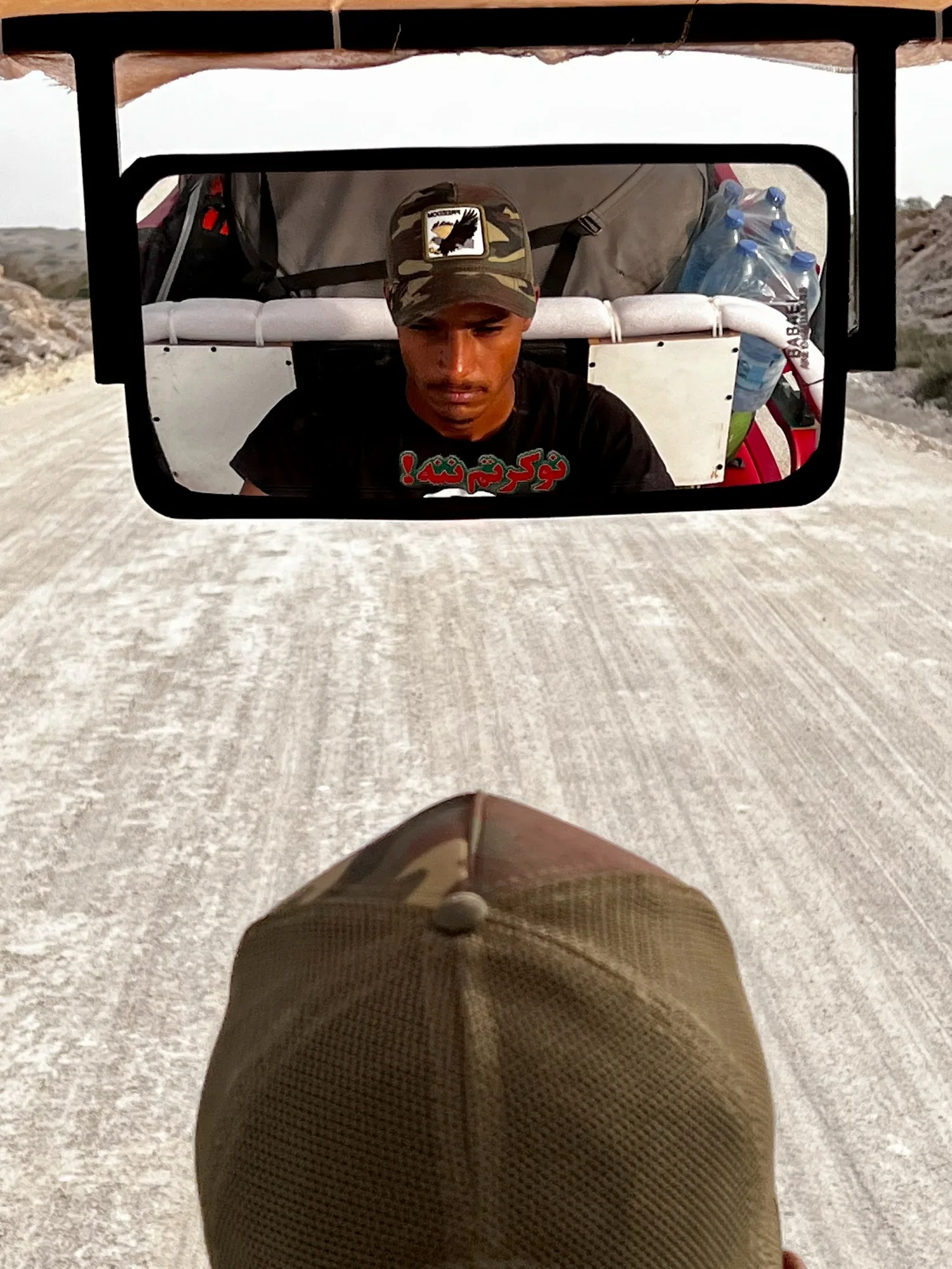 A driver's face framed in the rickshaw mirror.