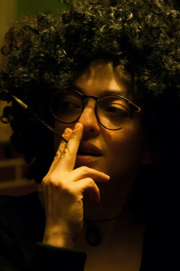 Warm lamplight, finger to the lips, the curls catching the light.