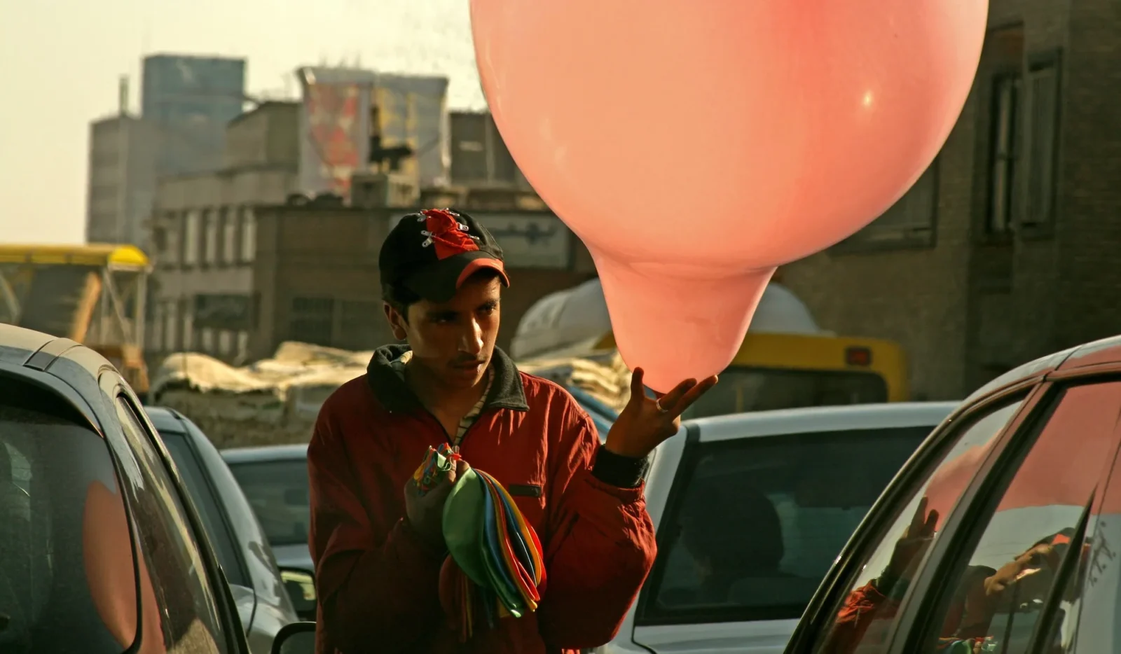 A boy with a pink balloon between cars in traffic, last light.