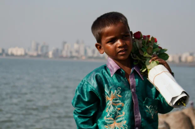 The rose seller with a rolled poster, the Mumbai skyline across the water.