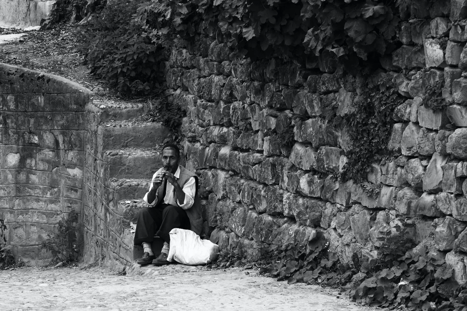 A figure crouched against a stone wall, small in the frame.
