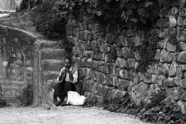 A figure crouched against a stone wall, small in the frame.