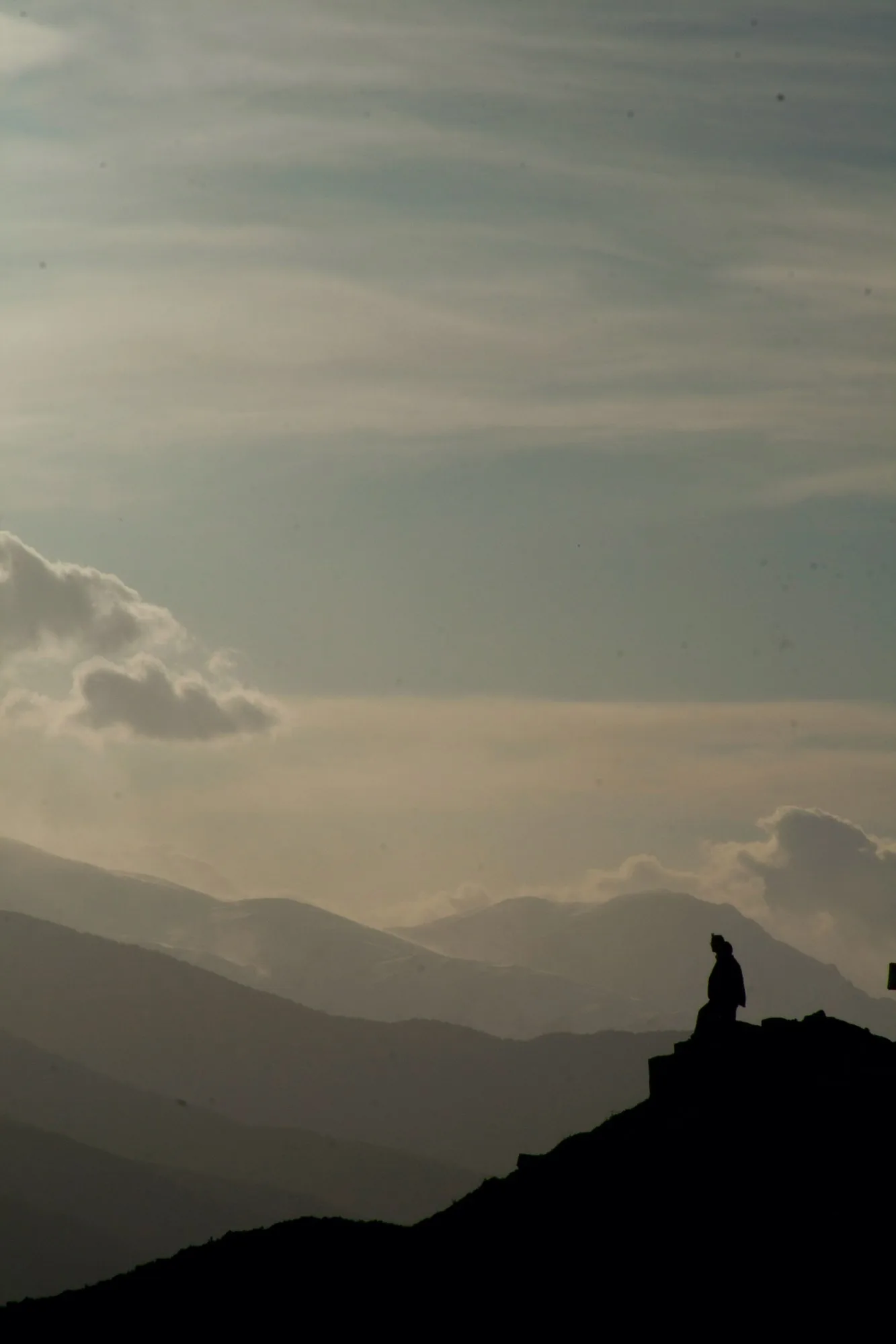 A figure on a rock above layered mist ridges.