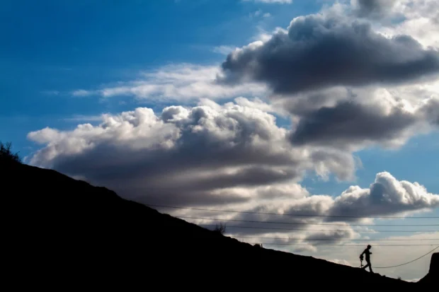 A black slope with one walker on it under a bank of cloud.