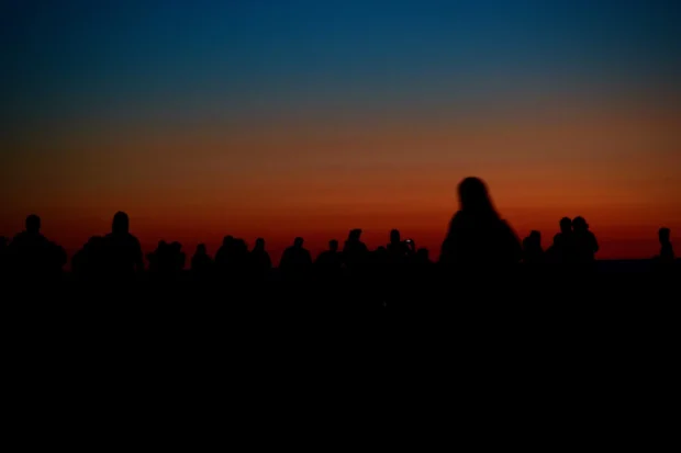 A row of people black against an orange band.